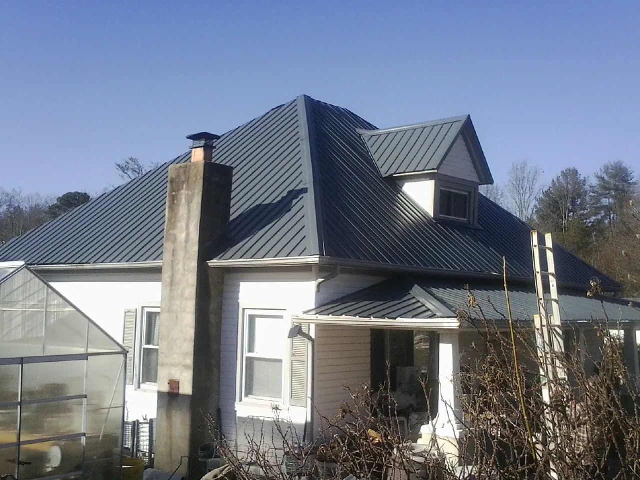 Dark blue standing seam metal roof on a white farmhouse with dormer — Slate & Tile Roof Repair by Roofing Brothers in Fultondale