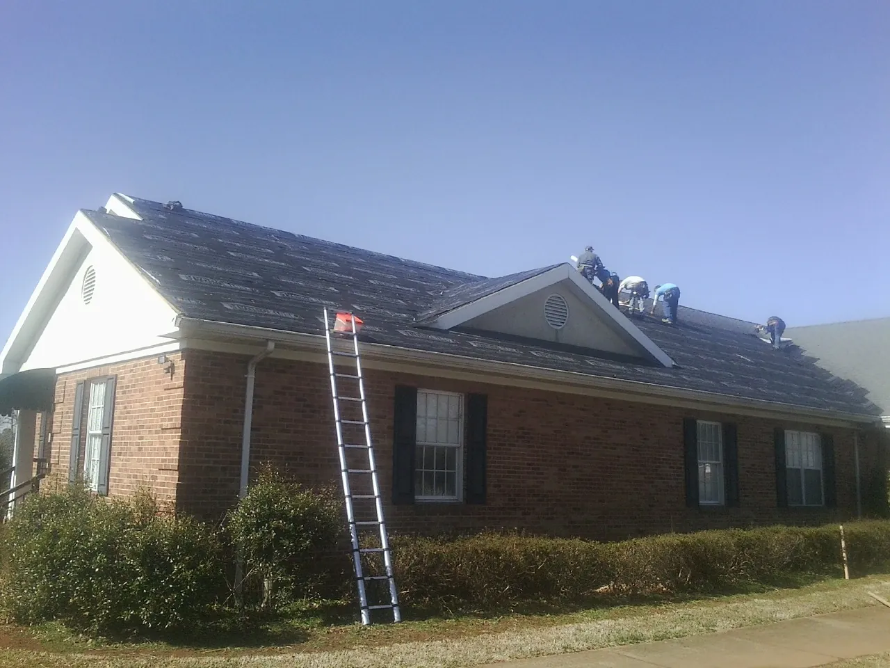 Crew tearing shingles off a brick ranch roof with a ladder set — Emergency Roof Repair work by our crew in Fultondale