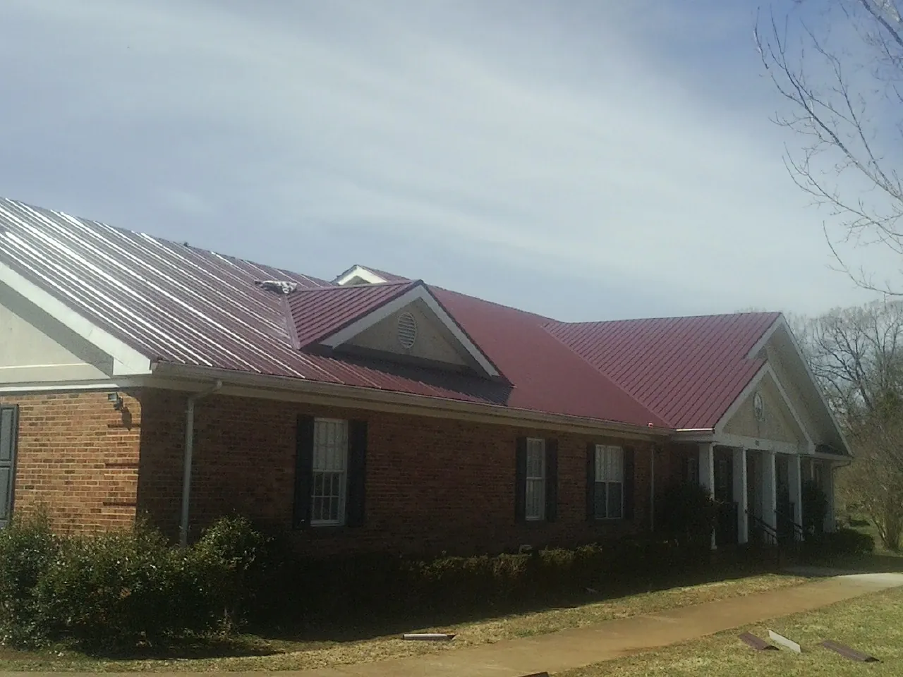 Red metal roof with gabled entries on a long brick building, from a Hail Damage Roof Repair job in Fultondale
