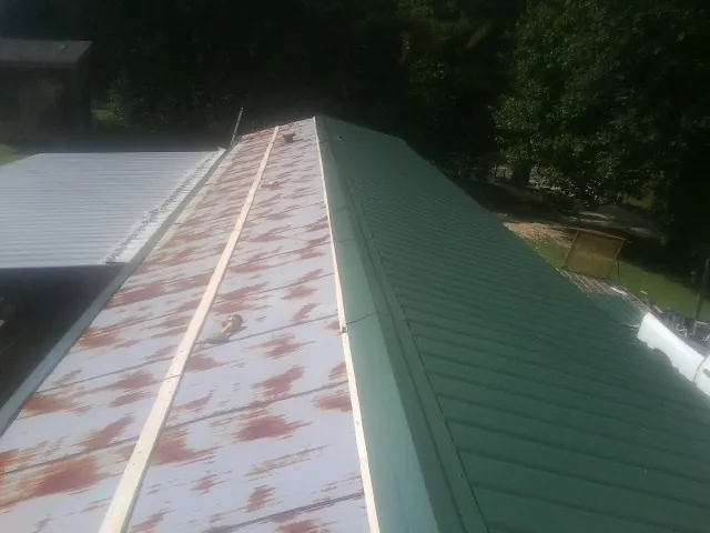 Old rusted panels beside newly installed green metal roofing — Wind Damage Roof Repair by Roofing Brothers in Fultondale