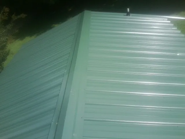 New green metal panels meeting at the ridge of a roof — Flat Roof Repair work by our crew in Fultondale