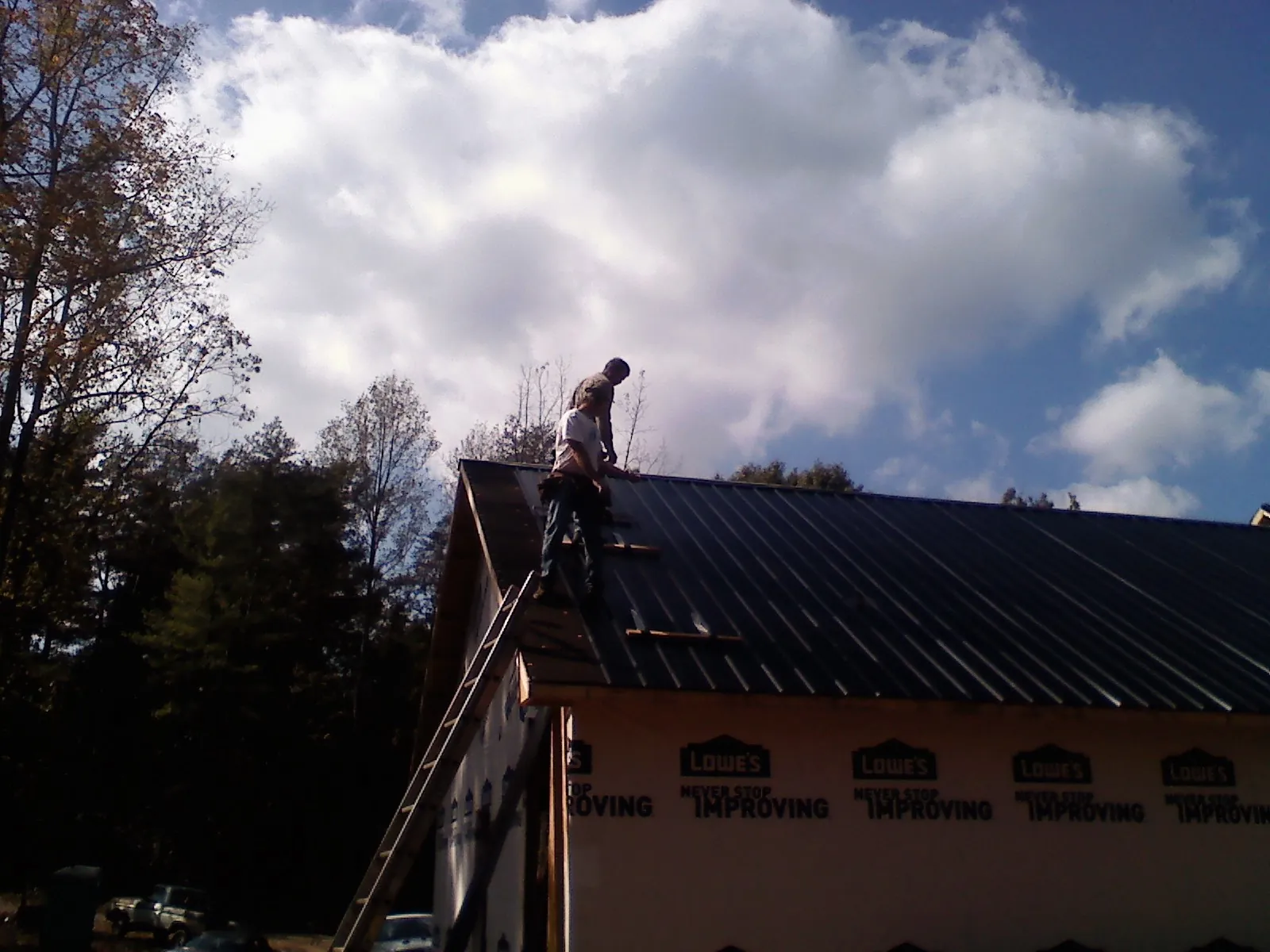 Roofer fastening dark metal panels high against a cloudy sky, from a Roof Inspection job in Fultondale
