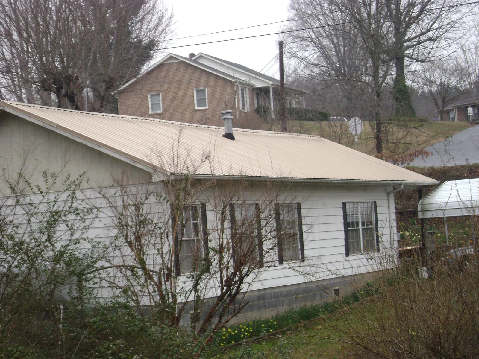 Tan metal roof on a white sided house set into a hillside — Commercial Roofing by Roofing Brothers in Fultondale